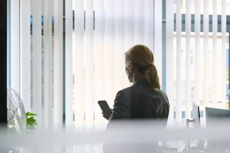  Eine Frau steht in einem Bürozimmer und telefoniert über ein Headset.