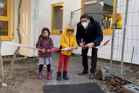Oberbürgermeister Thomas Hirsch schneidet mit zwei Kita-Kindern das Band zur Einweihung des Erweiterungsbaus durch. 