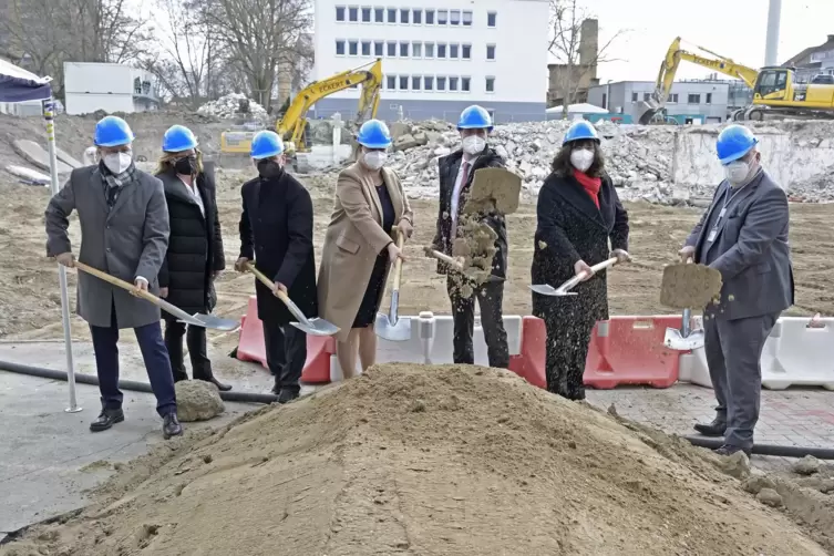 Mit Maske und Helm: Die Verantwortlichen schippen schon mal Sand.