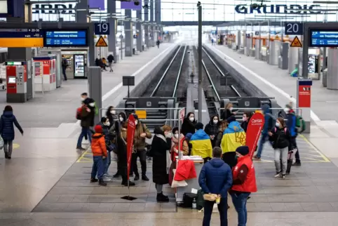 Helfer, in ukrainische Fahnen gehüllt, holen Flüchtlinge im Münchener Hauptbahnhof ab. 