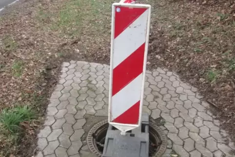 Ein geöffneter Kanaldeckel wird durch eine Warnbake notdürftig abgesichert.