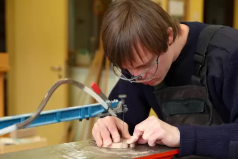 Philipp, ein Jugendlicher mit Trisomie 21, arbeitet an einer Dekupiersäge in der Goldbach- Werkstatt Nürnberg, eine Werkstatt fü