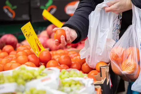 Eine Kundin begutachtet eine Tomate auf einem Wochenmarkt. Wegen der steigenden Inflation müssen viele Menschen in Deutschland d