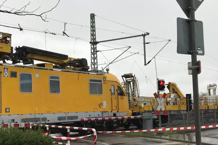 Ein Reparaturzug blockiert den Bahn&uuml;bergang. Rechts davon sieht man die Oberleitung herunterh&auml;ngen. 