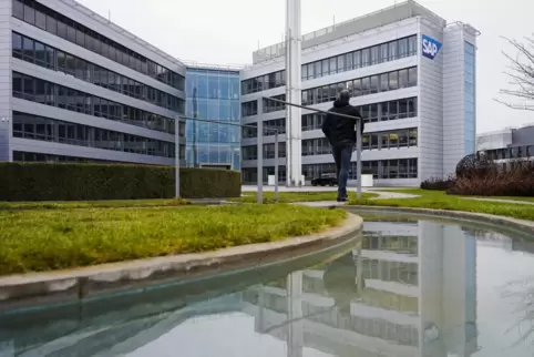 Ein Mann geht in Walldorf vor dem Hauptgebäude des Softwarekonzerns SAP an einem Wasserlauf, in dem sich das Gebäude spiegelt, ü