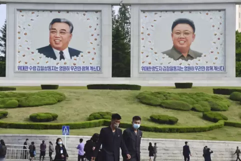 Menschen tragen Mund-Nasen-Schutz und gehen an Porträts der verstorbenen nordkoreanischen Führer Kim Il Sung und Kim Jong Il in 
