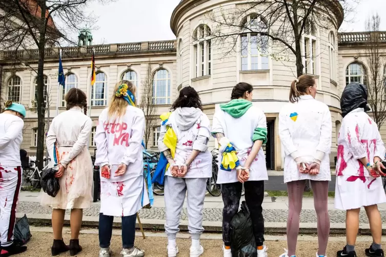 Frauen protestieren in Berlin in weißer Kleidung mit künstlichem Blut darauf sowie verbundenen Händen gegen die Gewalt an Frauen