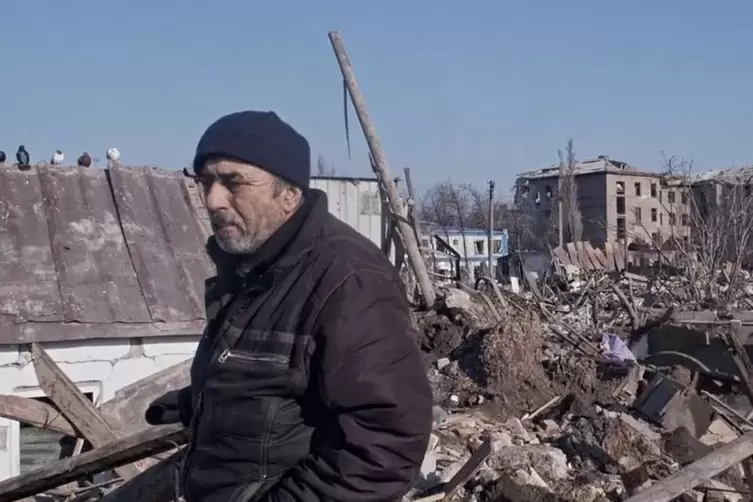 Êin Mann steht bei den Trümmern seines Hause.