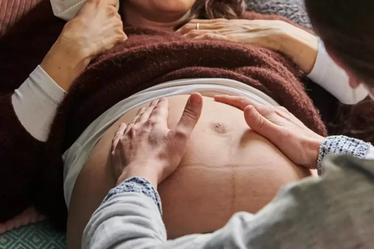 Eine Hebamme tastet den Bauch einer schwangeren Frau ab. 