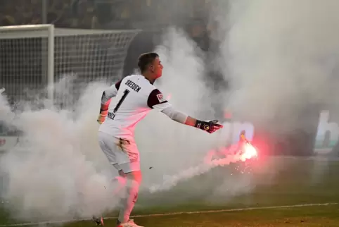 2022: Dresdens Torwart Kevin Broll beseitigt Pyrotechnik vom Rasen. Die Relegation ist ein Sicherheitsrisiko.