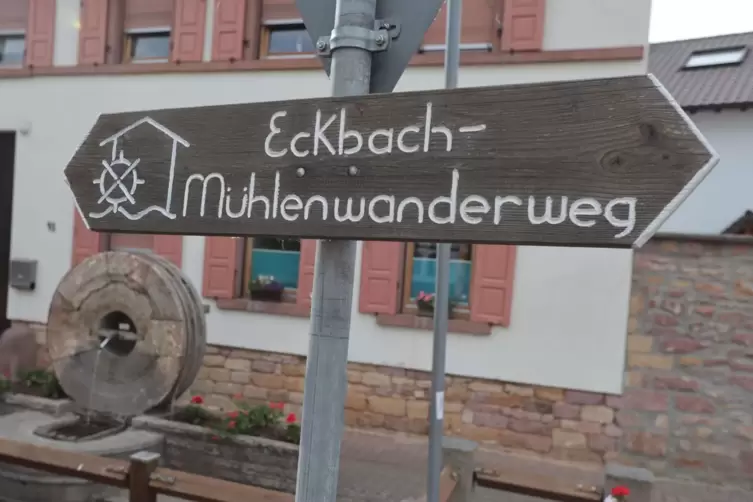 In Kleinkarlbach steht hinter einem Hinweisschild auf den Eckbach-Mühlenwanderweg passend ein Mühlrad auf einem Brunnen.