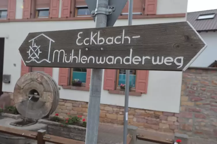 In Kleinkarlbach steht hinter einem Hinweisschild auf den Eckbach-M&uuml;hlenwanderweg passend ein M&uuml;hlrad auf einem Brunnen.