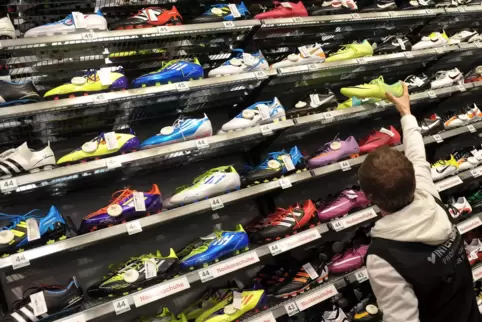 Ein Verkäufer in einem deutschen Sportfachgeschäft sucht den passenden Schuh für einen Kunden aus.