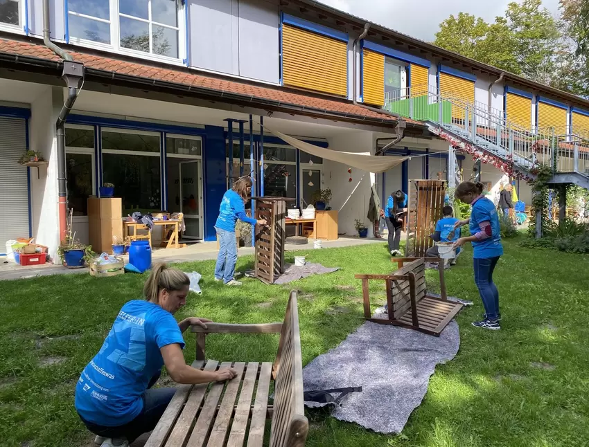 Im Garten der Integrativen Kita Sonnenblume machen sich die Eltern an den Zwischenwänden der Terrasse und den Bänken zu schaffen
