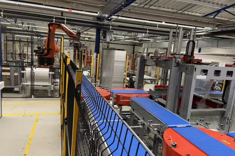 Die neue Verpackungsautomation: Über Bänder und Drehteller werden die Rollen transportiert und vom orangefarbenen Kran auf Palet