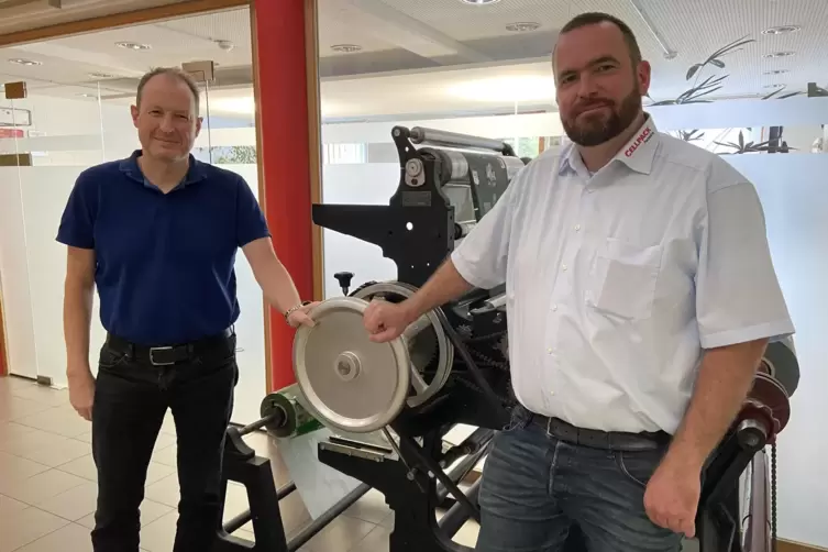 Standortleiter Jens Zobel (rechts) und Prokurist Heiko Jung an der im Foyer ausgestellten historischen Druckmaschine.