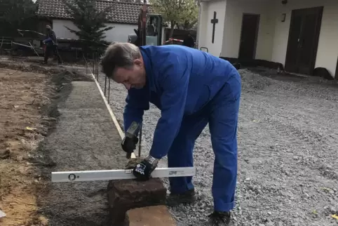 Der Ehrenamtler Oswald Alleborn mauert mit Sandsteinen die Abgrenzung des neuen Pflasters zu den Wiesengräbern. 