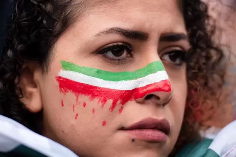 Eine Frau hat sich die blutende iranische Flagge ins Gesicht gemalt.