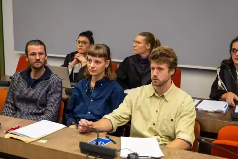 Drei angeklagte Klimaaktivisten sitzen zu Beginn des Eilverfahrens vor ihren Anwältinnen im Gerichtssaal.