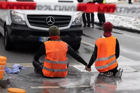 Zwei Klimaaktivisten nehmen an einer Protestaktion der Gruppe "Letzte Generation" teil, indem sie versuchen sich auf einer Straß