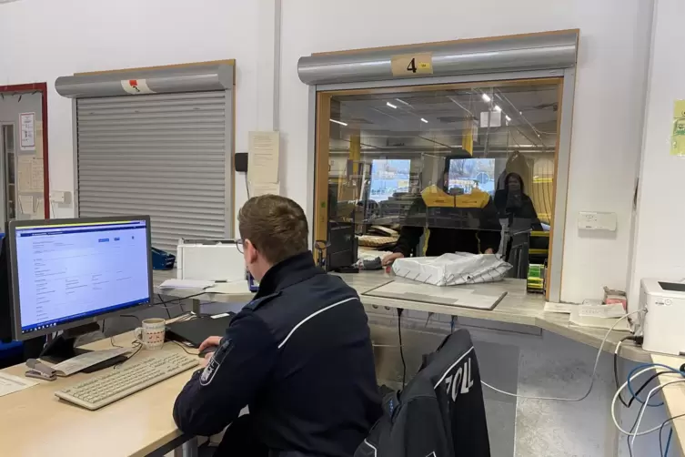 Ein Zollbeamter kontrolliert die Begleitunterlagen zu einem P&auml;ckchen. Der DHL-Mitarbeiter wird es kurz danach &ouml;ffnen. 