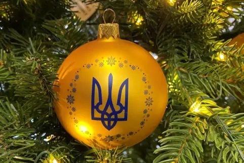 An einem geschmückten Baum in einem Geschäft hängt eine Kugel in den ukrainischen Nationalfarben Blau und Gelb mit dem Dreizack 