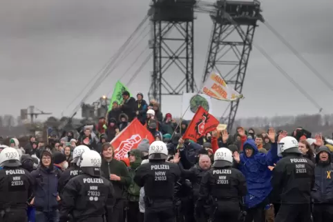 Polizisten und Demonstranten mit erhobenen Händen stehen sich am Rande des Braunkohletagebaus bei Lützerath gegenüber, im Hinter