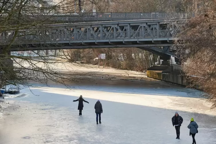 Menschen spazieren auf einem zugefrorenen Kanal in Hamburg. Unter Brücken kann dies gefährlich werden. 