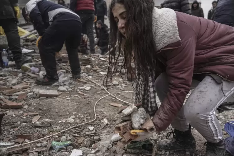Eine Frau räumt Trümmer von einem zerstörten Gebäude in Gaziantep, während sie mit Notfallteams nach verschütteten Menschen such