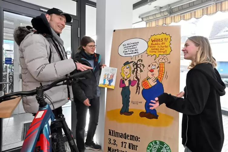 Steffen Boiselle und Greta Alberti und Hanna Fuhrbach stellen das Plakat im Fahrradladen auf. 