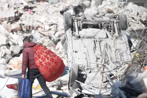 Türkei, Antakya: Ein Mann trägt seine Habseligkeiten über Erdbebentrümmern. 