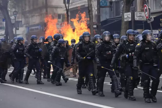 Angehörige der Bereitschaftspolizei gehen in Paris an brennendem Müll vorbei.