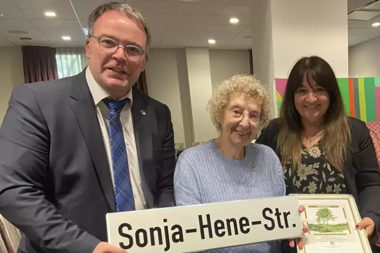 Bürgermeister Tobias Meyer und Frieda Frick übergeben Vera Heuberger ein Straßenschild mit dem Namen ihrer Schwester Sonja Hene.