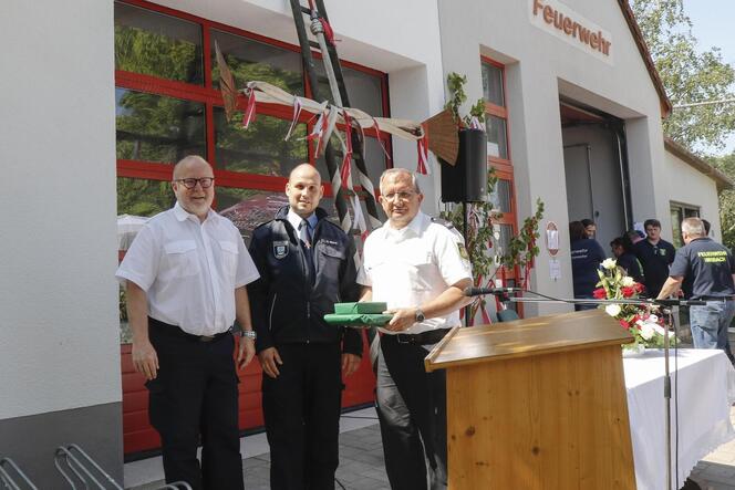Wehrführer Kevin Wiley (Bildmitte) wird beglückwünscht von Kreisfeuerwehrinspekteur Eberhard Fuhr (rechts) und Bürgermeister Rud