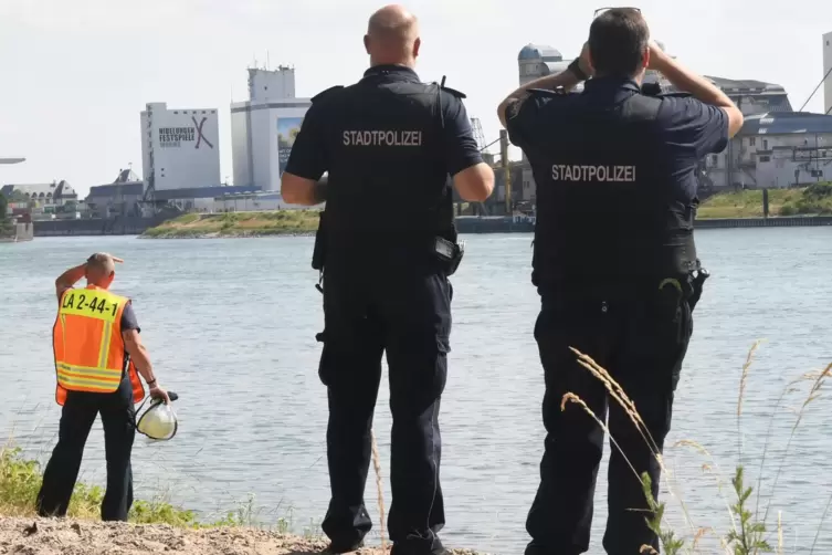Vom Ufer aus suchen Polizisten nach zwei Schwimmern im Rhein.
