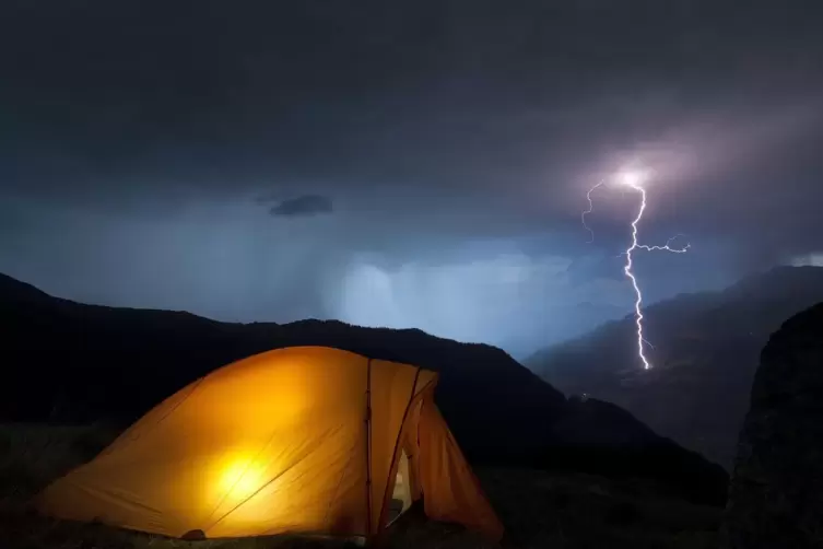 Ein Camper sucht Schutz in seinem Zelt, während nicht weit davon ein Blitz einschlägt. 