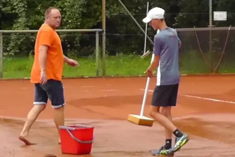 Markus Schmitt und Luca Scheid saugen mit gro&szlig;en Schw&auml;mmen das Regenwassre vom Platz.