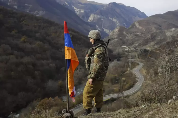 Ein armenischer Soldat steht neben der Flagge von Berg-Karabachs auf einer Anhöhe, von wo aus er die Straße kontrolliert. 