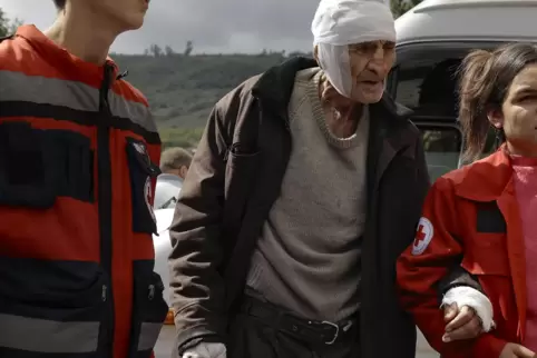 Ein verwundeter, über 80 Jahre alter Mann aus Berg-Karabach wird bei seiner Ankunft in Armenien von jungen Helfern empfangen. 