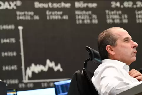 Risiken streuen: Ein Aktienhändler auf dem Parkett der Frankfurter Wertpapierbörse, im Hintergrund der Kursverlauf des Dax. 