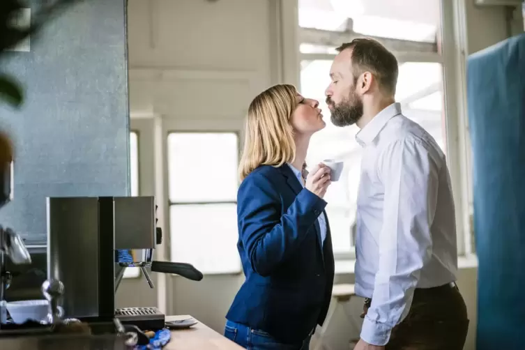 Zwei Personen küssen sich in einem Büro
