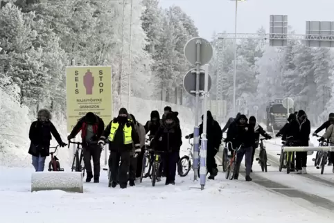 Finnische Grenzschutzbeamte eskortieren Migranten mit Fahrrädern am Grenzübergang in Salla. 