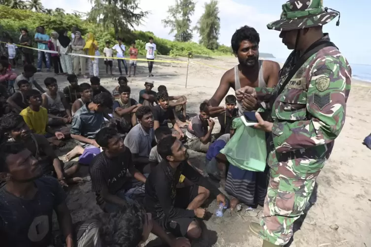 Ein Soldat überprüft Ausweise von Rohingya, nachdem sie am Sonntag an einem Strand in Indonesien gelandet sind. Zwei Boote mit H