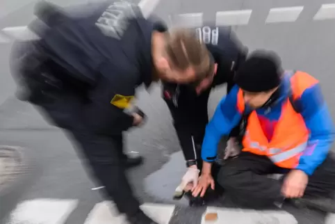  Polizisten versuchen festgeklebte Hände von Aktivisten der Gruppierung «Letzte Generation» in Hannover mit Speiseöl von der Str
