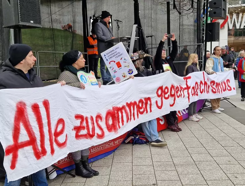 Plakat vor der Bühne am Berliner Platz. Am Mikro: Ibrahim Yetkin, stellvertretender Vorsitzender des Beirats für Migration und I