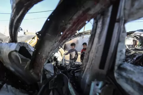 Palästinensische Kinder in Rafah vor einem ausgebrannten Wrack nach einem israelischen Luftangriff. 
