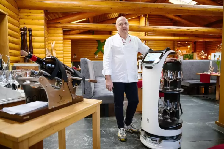 André Folschweiller, Chef des Restaurants Grill au Bois, steht neben einem Roboter, der Gläser zu Tischen fährt. Das Restaurant 
