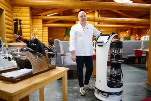 André Folschweiller, Chef des Restaurants Grill au Bois, steht neben einem Roboter, der Gläser zu Tischen fährt. Das Restaurant 