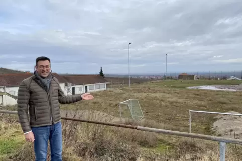 Ortschef Christian Weber zeigt auf den Sportplatz in Burrweiler. Das Sportheim links im Hintergrund soll abgerissen werden.