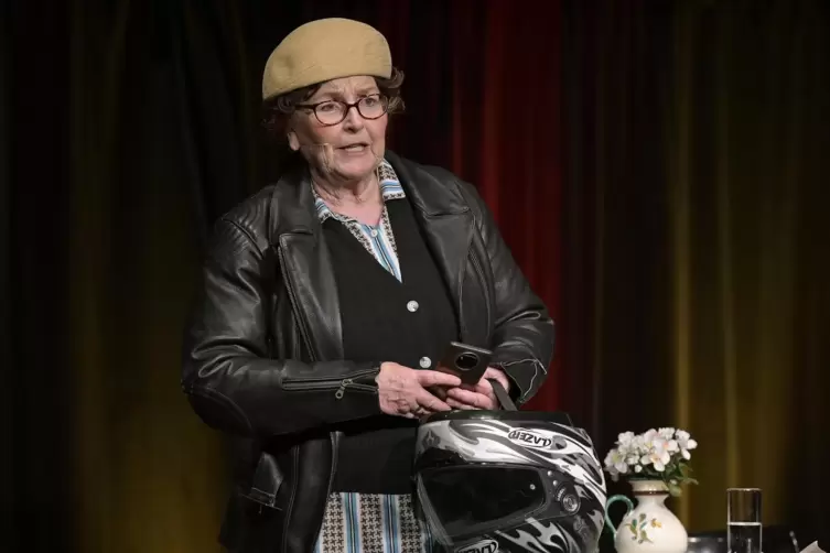 Dunkle Lederjacke über der bunten Kittelschürze, altmodische Mütze und ein Motorradhelm in der Hand: Alice Hoffmann in der Klaps